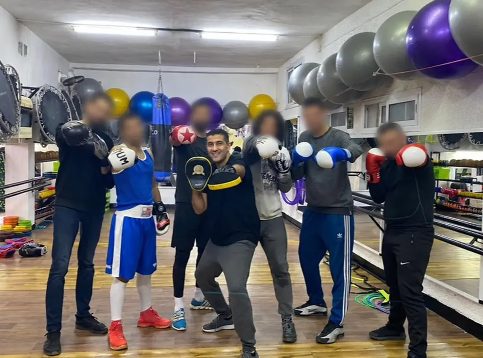 Kamel au centre d'un groupe de boxe aux visages floutés